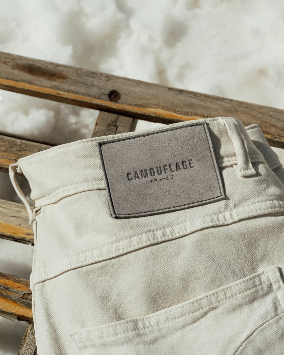 Close-up of Camouflage premium denim jeans with signature label and hardware